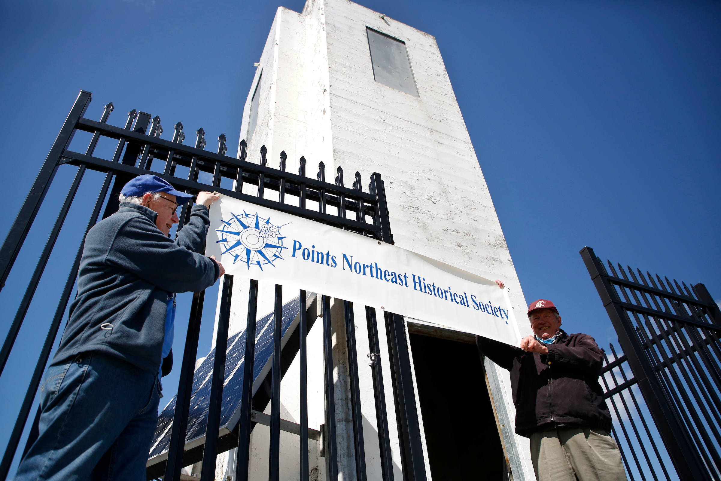 photo of men holding a sign in front of lighthouse