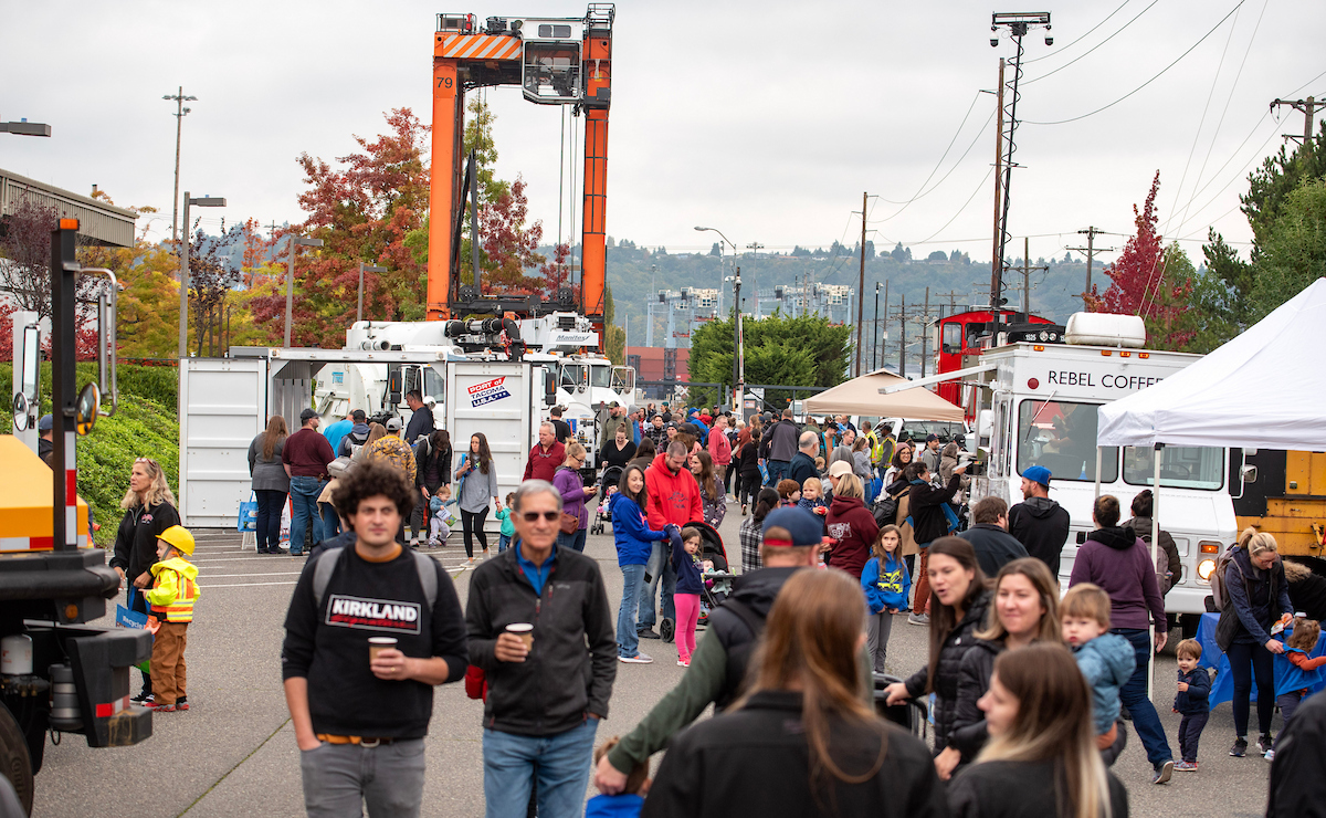 A panning shot of a crowd in a parking lot with a crane in the background. 