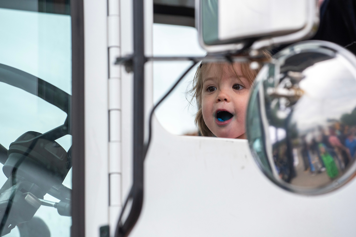 A small girl sits in the cab of a white truck. 