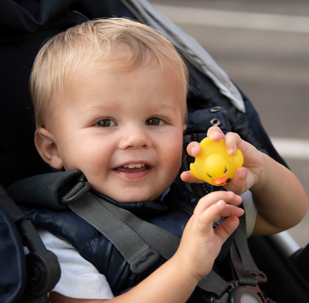 A toddler in a stroller holds up a rubber duck.