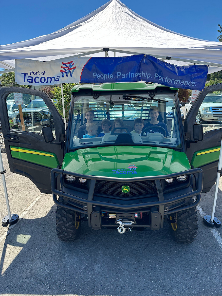 A group of children sit in a John Deere vehicle in front of a Port of Tacoma sign.