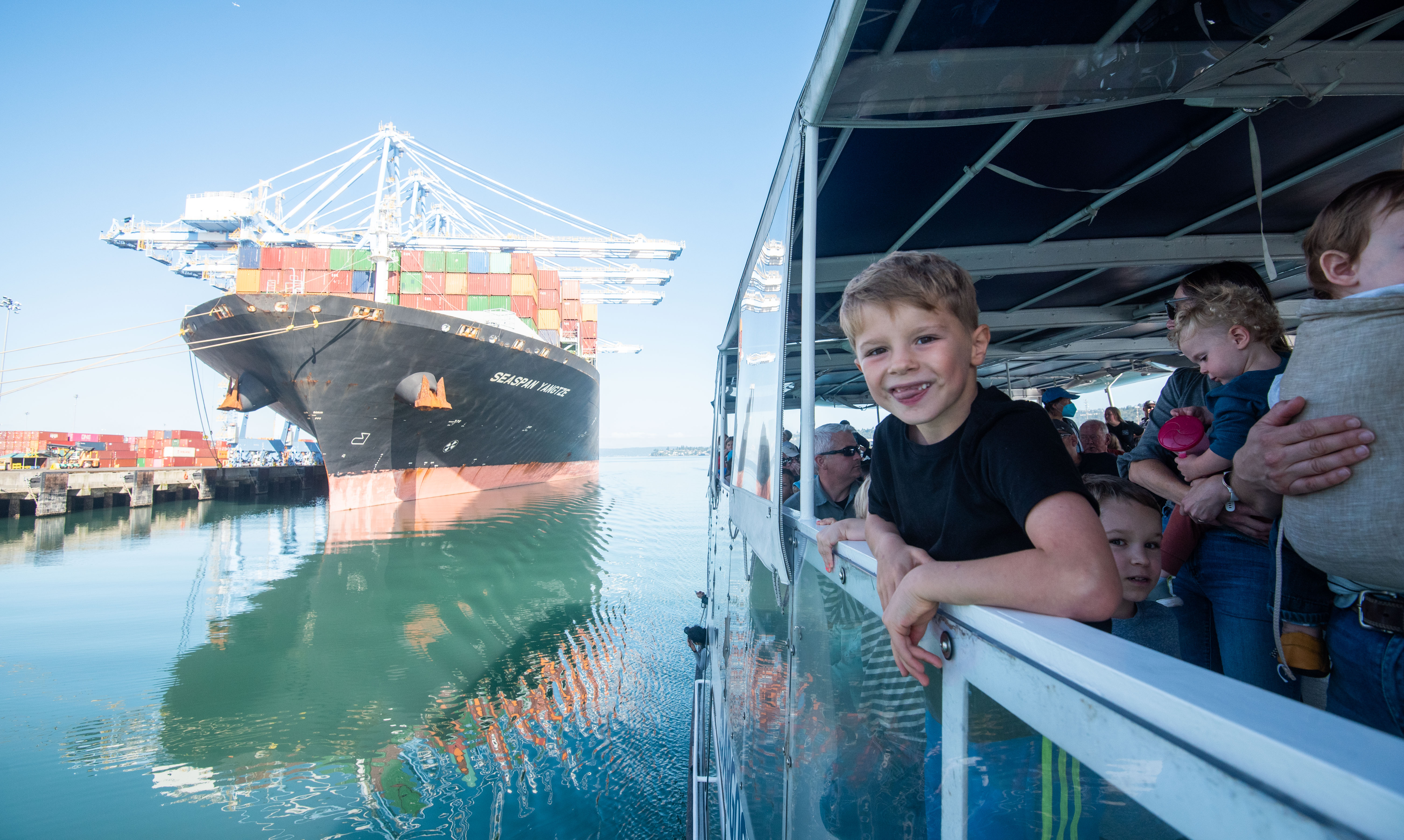 A young boy leans over the railing of a boat moving along a waterway. 