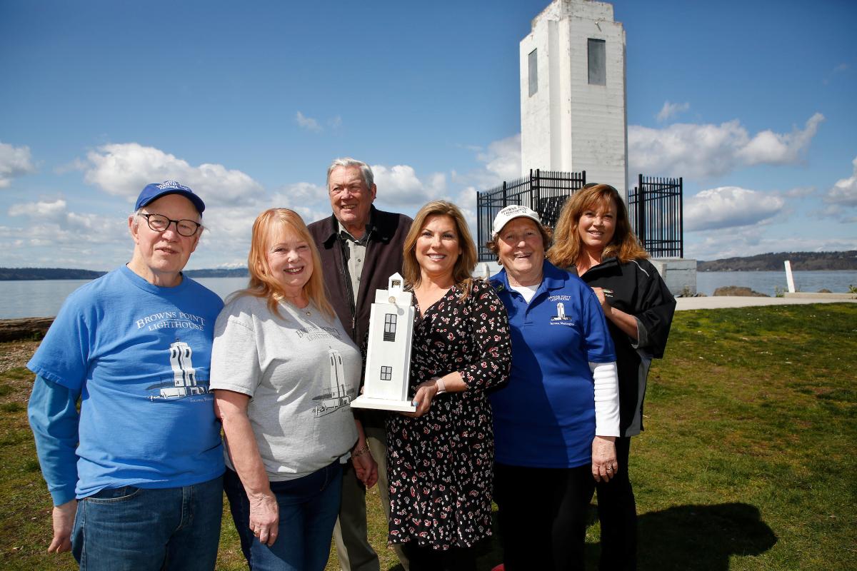 a photo of group of women and men holding a model of the lighthouse and smiling